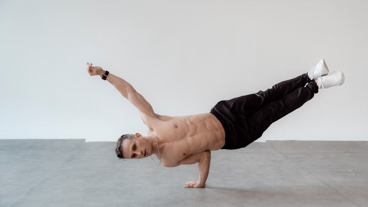 Athletic man in a one-handed handstand pose indoors, displaying strength and balance.
