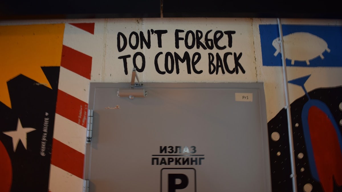 Graffiti on wall above door says "don't forget to come back"